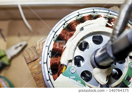 Disassembled electric bicycle motor hub featuring visible copper windings and hall sensor circuit board during maintenance process for e-bike repair and technical mechanical inspection 140764375