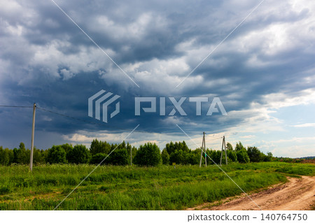 Massive dark storm clouds loom over a lush green meadow and rural dirt road, creating a dramatic and moody atmosphere before the heavy rain begins in the countryside Massive dark storm clouds loom over a lush green meadow and rural dirt road, creating a dramatic and moody atmosphere before the heavy rain begins in the countryside 140764750