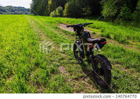 Electric fat bike parked on a dirt path crossing a lush green meadow, summer sunny day with vibrant nature background, eco-friendly transport adventure in the countryside outdoors Electric fat bike parked on a dirt path crossing a lush green meadow, summer sunny day with vibrant nature background, eco-friendly transport adventure in the countryside outdoors 140764770