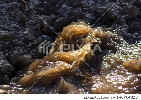 Swirling muddy spring stream water, frothy and turbulent. Golden brown foam dances on swift currents, capturing the raw power of nature's flow Swirling muddy spring stream water, frothy and turbulent. Golden brown foam dances on swift currents, capturing the raw power of nature's flow 140764828