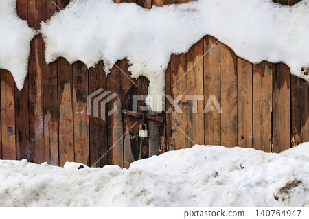 Weathered wooden garage doors partially covered with melting snow banks and a dangling padlock Weathered wooden garage doors partially covered with melting snow banks and a dangling padlock 140764947