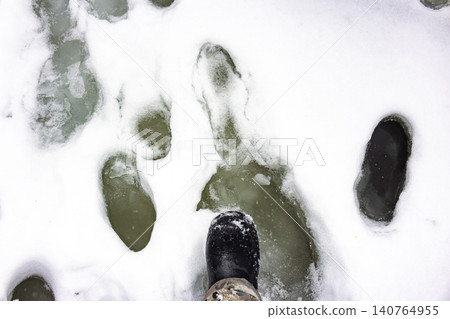 Precarious late-winter river ice, showing deep footprints and a submerged boot, a stark warning of melting conditions and hazardous thin ice Precarious late-winter river ice, showing deep footprints and a submerged boot, a stark warning of melting conditions and hazardous thin ice 140764955