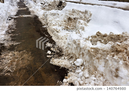 Dirty sidewalk after snow plowing shows melting slushy snow banks and wet pavement Dirty sidewalk after snow plowing shows melting slushy snow banks and wet pavement 140764980
