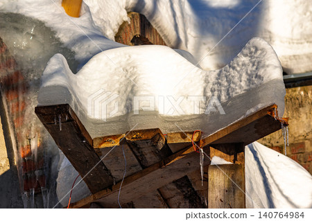 Heavy snow and ice cap rough wooden construction planks, with melting drips forming icicles in bright winter sun Heavy snow and ice cap rough wooden construction planks, with melting drips forming icicles in bright winter sun 140764984