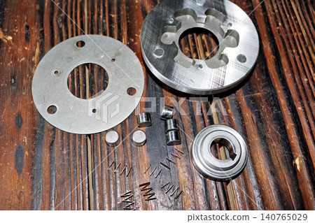Disassembled e-bike motor sprag clutch mechanism with steel rollers and small springs laid out on a rustic wooden table after thorough cleaning and maintenance Disassembled e-bike motor sprag clutch mechanism with steel rollers and small springs laid out on a rustic wooden table after thorough cleaning and maintenance 140765029