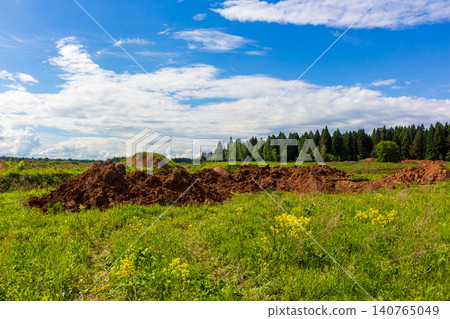 Large mounds of raw excavated soil sitting in a vibrant green meadow under a bright sunny sky with fluffy clouds, demonstrating landscape alteration and construction site preparation Large mounds of raw excavated soil sitting in a vibrant green meadow under a bright sunny sky with fluffy clouds, demonstrating landscape alteration and construction site preparation 140765049