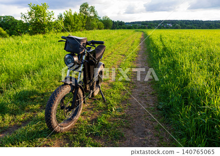 Modern electric fat bike parked on a narrow dirt path through a vibrant summer meadow with lush green grass during golden hour sunset light, outdoor travel adventure concept Modern electric fat bike parked on a narrow dirt path through a vibrant summer meadow with lush green grass during golden hour sunset light, outdoor travel adventure concept 140765065