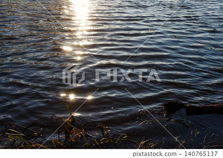 Vibrant sun sparkles shimmer brightly on the dark, deep water surface. Dynamic natural background texture with mesmerizing light reflections and flowing ripples Vibrant sun sparkles shimmer brightly on the dark, deep water surface. Dynamic natural background texture with mesmerizing light reflections and flowing ripples 140765137