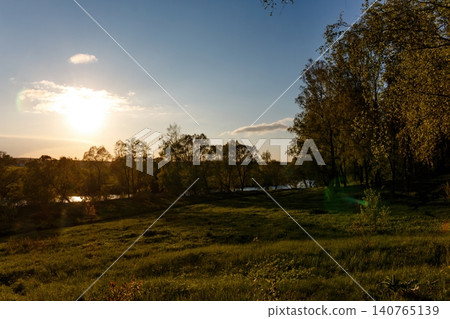Vibrant sunset illuminates a tranquil green field and shadowy trees by the river. Perfect nature backdrop Vibrant sunset illuminates a tranquil green field and shadowy trees by the river. Perfect nature backdrop 140765139