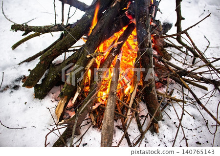 Vibrant flames fiercely embrace dark firewood, casting a warm, inviting glow on the crisp, white snow. A rustic winter campfire, perfect for cozy outdoor adventures Vibrant flames fiercely embrace dark firewood, casting a warm, inviting glow on the crisp, white snow. A rustic winter campfire, perfect for cozy outdoor adventures 140765143