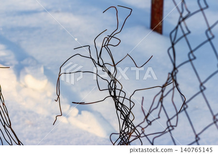 Rusted, twisted wires of a broken chain-link fence create an intricate, abstract pattern against pristine winter snow, bathed in soft evening sunlight Rusted, twisted wires of a broken chain-link fence create an intricate, abstract pattern against pristine winter snow, bathed in soft evening sunlight 140765145