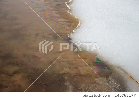 Vibrant, toxic oil slick paints a dirty river, merging with melting snow. A harsh environmental warning of pollution and ecological damage 140765177