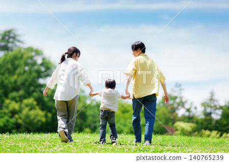 A family of three walking hand in hand in the park. A family of three walking hand in hand in the park. 140765239