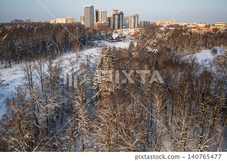 Stunning aerial view of a frosty winter forest, snow-covered trees reaching towards a distant cityscape under golden hour light, contrasting nature and urban development Stunning aerial view of a frosty winter forest, snow-covered trees reaching towards a distant cityscape under golden hour light, contrasting nature and urban development 140765477