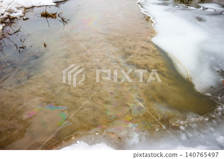 Icy winter river contaminated by a vivid rainbow oil slick. This toxic fuel discharge represents stark environmental pollution and water contamination, a serious nature blight Icy winter river contaminated by a vivid rainbow oil slick. This toxic fuel discharge represents stark environmental pollution and water contamination, a serious nature blight 140765497