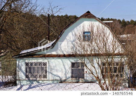 Charming vintage cottage in a rural village during early spring, featuring weathered walls and bare tree branches under a clear blue sky, capturing a peaceful rustic seasonal transition Charming vintage cottage in a rural village during early spring, featuring weathered walls and bare tree branches under a clear blue sky, capturing a peaceful rustic seasonal transition 140765546