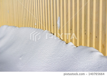 Bright snowdrift meeting a textured, pale yellow corrugated metal wall under crisp daylight Bright snowdrift meeting a textured, pale yellow corrugated metal wall under crisp daylight 140765664