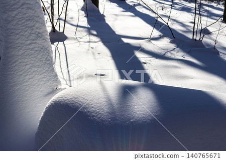 Deep snow drifts catch crisp winter sun, casting dramatic, deep blue shadows across a pristine forest floor Deep snow drifts catch crisp winter sun, casting dramatic, deep blue shadows across a pristine forest floor 140765671
