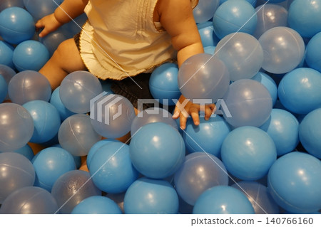 A part of the body of a one-year-old toddler playing in a blue ball pit. Indoor playground. A part of the body of a one-year-old toddler playing in a blue ball pit. Indoor playground. 140766160