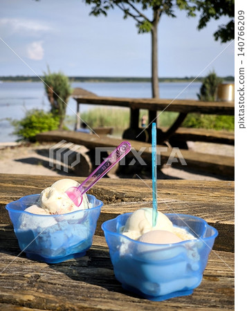 Two cups of ice cream on a wooden table by the lake. Two cups of ice cream on a wooden table by the lake. 140766209