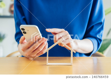 A young woman's hands holding a model house and a smartphone. A young woman's hands holding a model house and a smartphone. 140766459