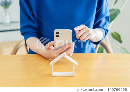 一位年輕女子的手拿著一個房屋模型和一部智慧型手機。 140766466