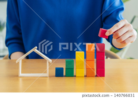 A young woman's hands as she looks at a model house and building blocks. A young woman's hands as she looks at a model house and building blocks. 140766831