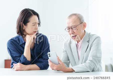 An elderly man with a troubled expression learns to use a smartphone. 140766845