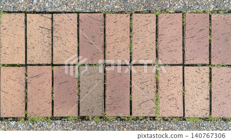 A texture of a red brick path with gravel borders and weeds. A texture of a red brick path with gravel borders and weeds. 140767306