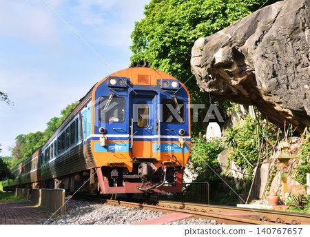 Thai SRT Train Passing Large Rock Cliff and Shrine in Kanchanaburi Thai SRT Train Passing Large Rock Cliff and Shrine in Kanchanaburi 140767657