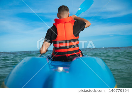Man paddles a kayak in clear blue waters on a sunny day Man paddles a kayak in clear blue waters on a sunny day 140770594