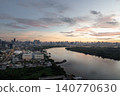 The wide, serene river acts as a mirror to the dawn, gracefully snaking its way through a vast landscape where nature meets civilization. Soft pastel hues of pink, gold, and lavender paint the clouds 140770630