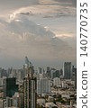 A modern metropolis unfolds beneath a dramatic, cloud-swept sky. Sleek skyscrapers rise above dense urban neighborhoods, blending contemporary design with bustling city life. In the distance, a 140770735