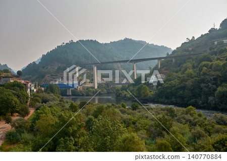 Galician village of Peares with modern viaducts and a train bridge crossing the river in a natural mountain landscape Galician village of Peares with modern viaducts and a train bridge crossing the river in a natural mountain landscape 140770884