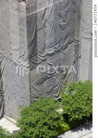 It is a building under remodeling that is covered by a screen. It is a building under remodeling that is covered by a screen. 140771454