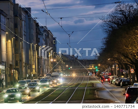 Urban dusk street with moving vehicles. City nightlife filled with glowing lights and quiet traffic Urban dusk street with moving vehicles. City nightlife filled with glowing lights and quiet traffic 140771734