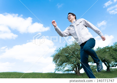 A male engineer in work clothes takes a big leap under a blue sky, symbolizing a successful leap. A male engineer in work clothes takes a big leap under a blue sky, symbolizing a successful leap. 140771747