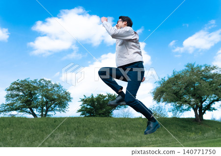 A male engineer in work clothes takes a big leap under a blue sky, symbolizing a successful leap. A male engineer in work clothes takes a big leap under a blue sky, symbolizing a successful leap. 140771750