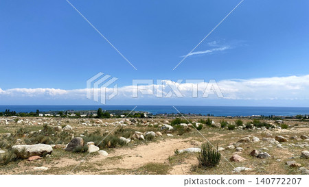 View of the bright blue strip of Lake Issyk-Kul in Kyrgyzstan. Beautiful summer landscape. Travel to Kyrgyzstan. A rocky rural trail. Amazing panorama of Lake Issyk-kul. Trekking and hiking in View of the bright blue strip of Lake Issyk-Kul in Kyrgyzstan. Beautiful summer landscape. Travel to Kyrgyzstan. A rocky rural trail. Amazing panorama of Lake Issyk-kul. Trekking and hiking in 140772207