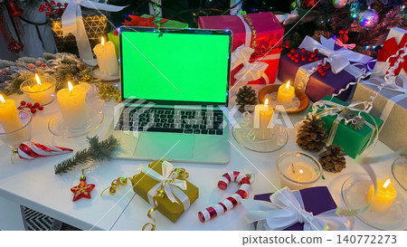 Christmas concept of advertising on a computer. Laptop with a chroma key on the screen is on the New Year's table. Beautifully packaged gift boxes, burning candles, cones, confetti Christmas concept of advertising on a computer. Laptop with a chroma key on the screen is on the New Year's table. Beautifully packaged gift boxes, burning candles, cones, confetti 140772273