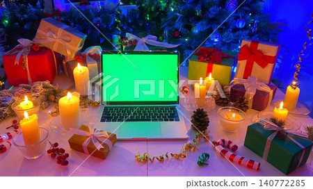 Gift boxes, burning candles, cones, confetti, a fir branch with red berries and striped caramel. Personal computer with a chroma key on the screen lies on the New Year's table. 140772285