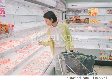 A young woman picks up a package of meat and chooses it in the meat section of a supermarket. A young woman picks up a package of meat and chooses it in the meat section of a supermarket. 140772319
