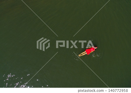 Aerial view of woman in red dress floats peacefully in a lake, embracing serenity and solitude Aerial view of woman in red dress floats peacefully in a lake, embracing serenity and solitude 140772958