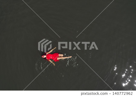 Aerial view of gorgeous woman in red dress floating on calm water Aerial view of gorgeous woman in red dress floating on calm water 140772962