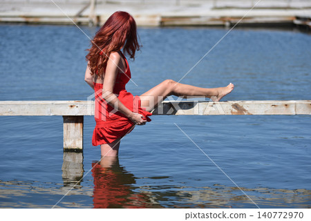 Back view of provocative woman win red dress showing her legs on poolside Back view of provocative woman win red dress showing her legs on poolside 140772970
