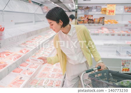 一位年輕的女顧客在超市肉品區彎腰挑選一包肉。 一位年輕的女顧客在超市肉品區彎腰挑選一包肉。 140773230