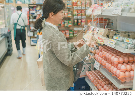 A middle-aged woman picks up eggs and checks them at the supermarket. A middle-aged woman picks up eggs and checks them at the supermarket. 140773235
