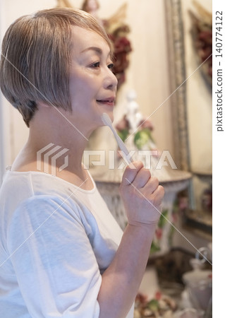 A senior woman brushing her teeth at the bathroom sink. A senior woman brushing her teeth at the bathroom sink. 140774122