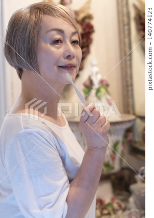 A senior woman brushing her teeth at the bathroom sink. A senior woman brushing her teeth at the bathroom sink. 140774123