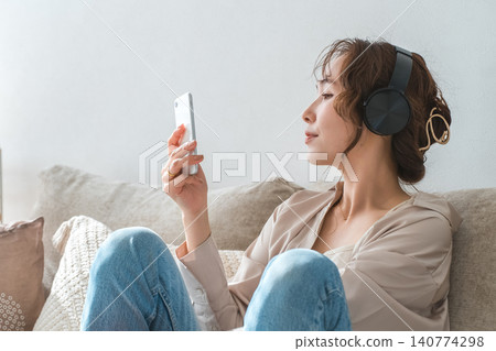 A relaxed woman sitting on a sofa at home, listening to music with headphones on. A relaxed woman sitting on a sofa at home, listening to music with headphones on. 140774298